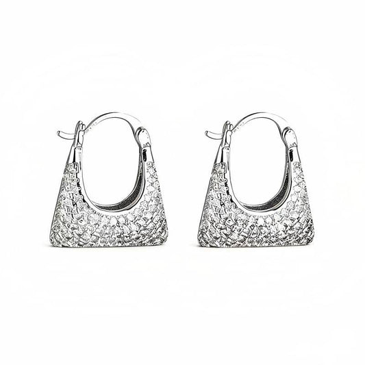 A product shot of MERCURY brand modern silver geometric hoop earrings sculpted in the shape of a miniature handbag or purse, featuring a detailed woven texture on the front and pavé-set with sparkling AAA Cubic Zirconia stones, isolated on a clear white background.