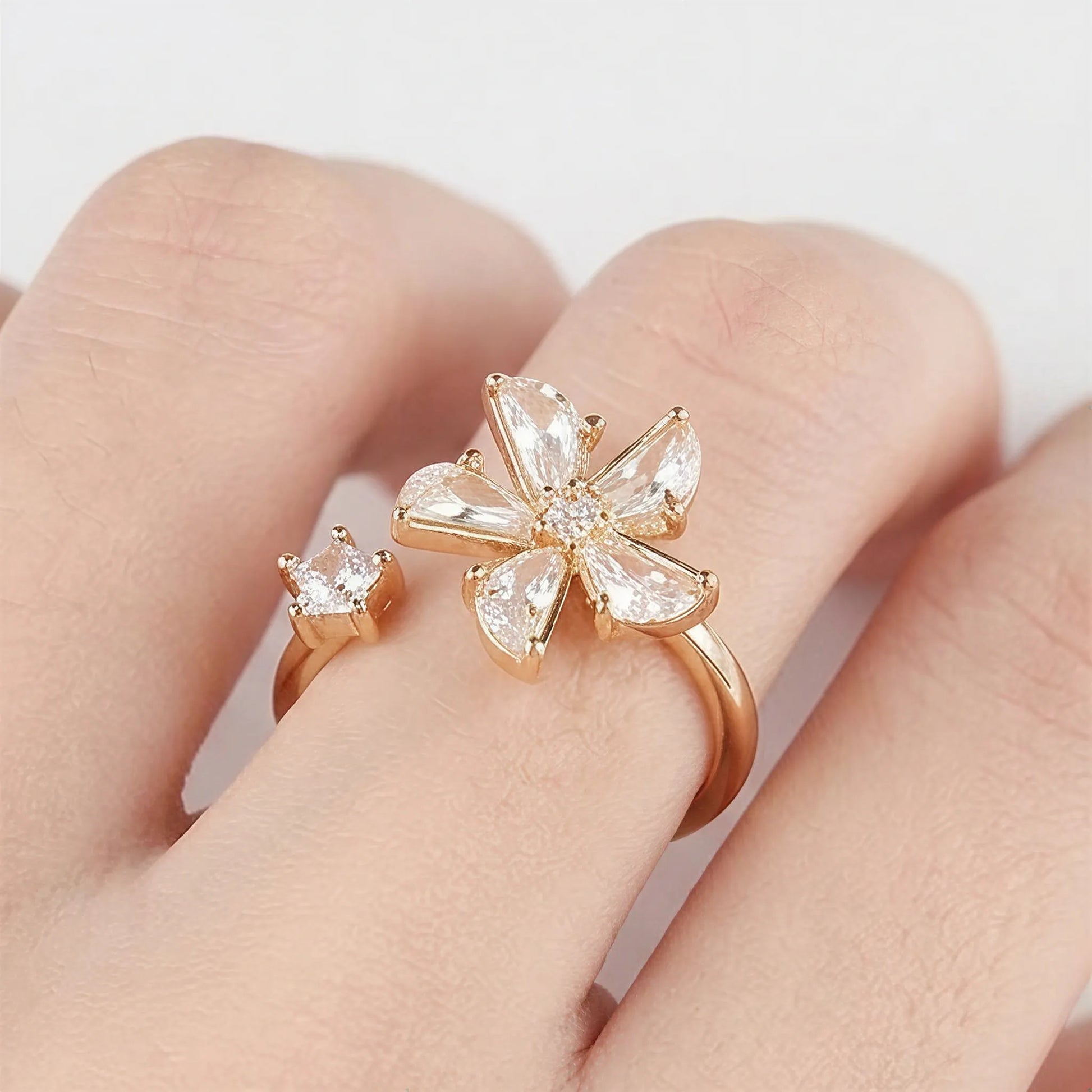 Close-up of a Mercury rose gold flower and star spinner ring on a finger, featuring sparkling AAA cubic zirconia on a minimalist white background.